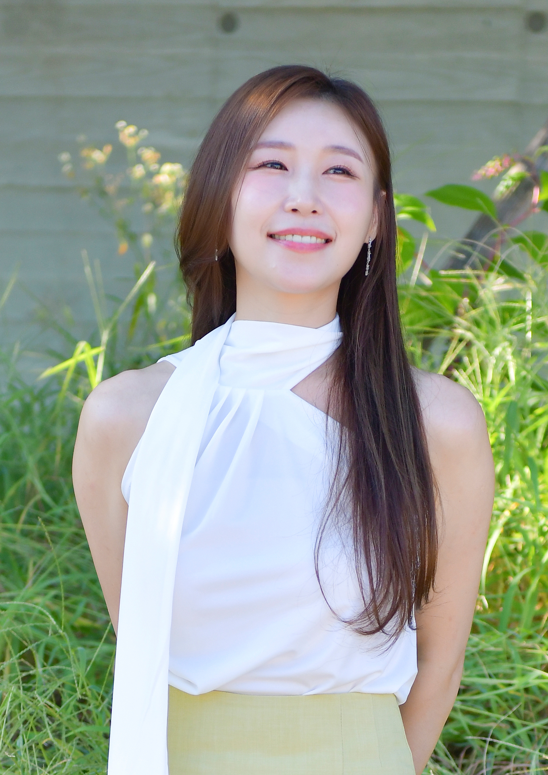 야외에서 흰색 무대 의상을 입고 미소 짓는 가수 이소나